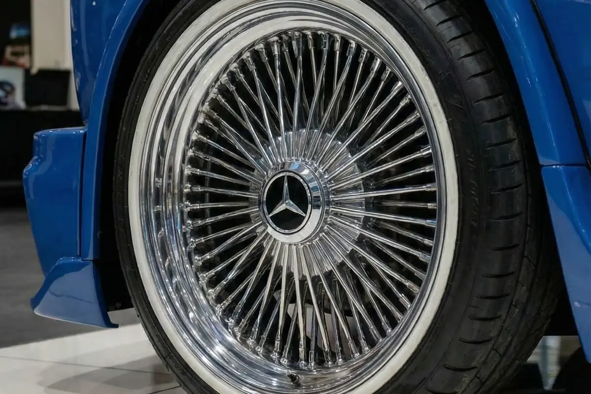 Detalhe da roda raiada cromada com pneu faixa branca e calota Mercedes-Benz no Kingpin azul.
