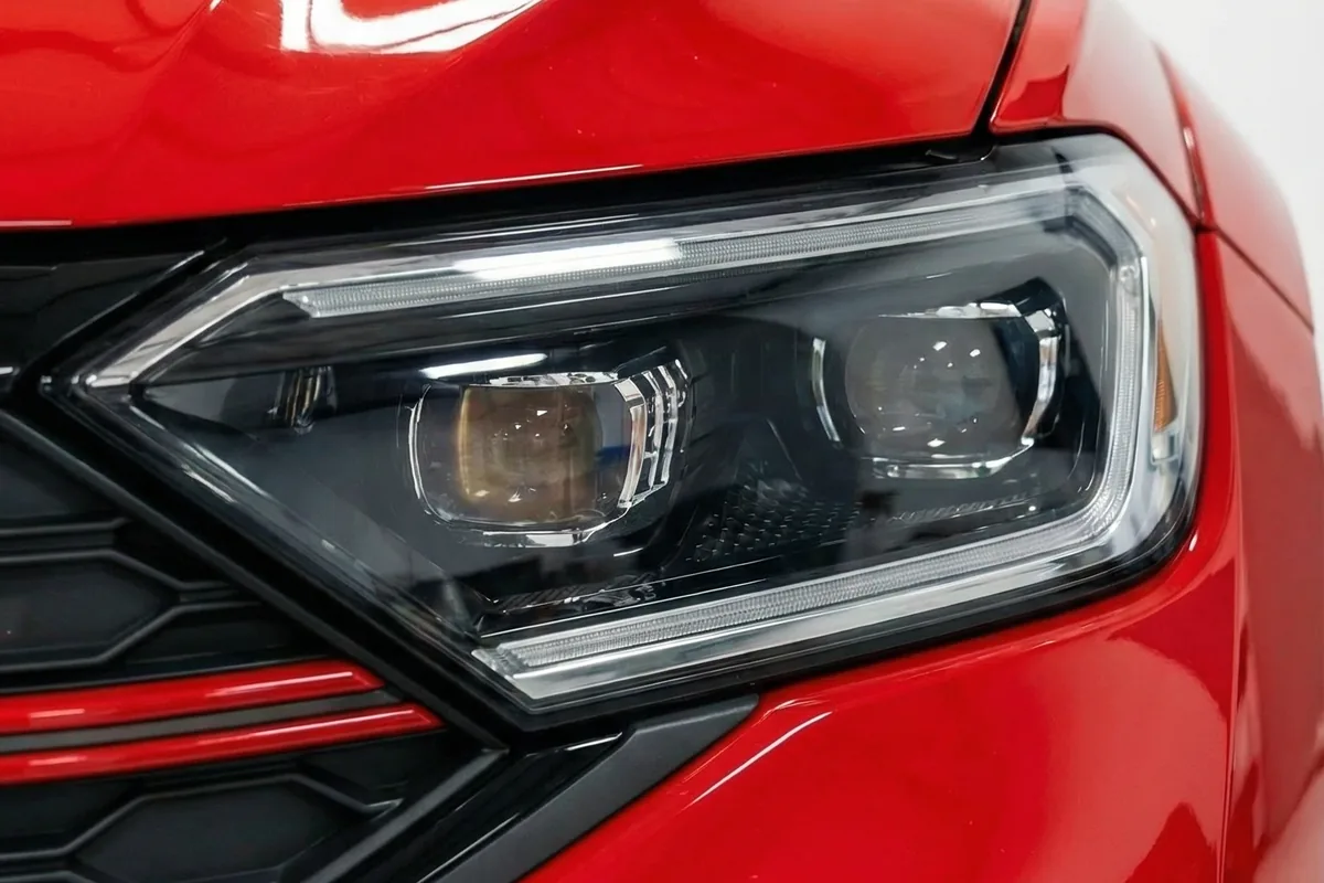 Detalhe do farol dianteiro esquerdo de LED da Volkswagen Brasilia GLI Restomod vermelha, com grade em segundo plano.