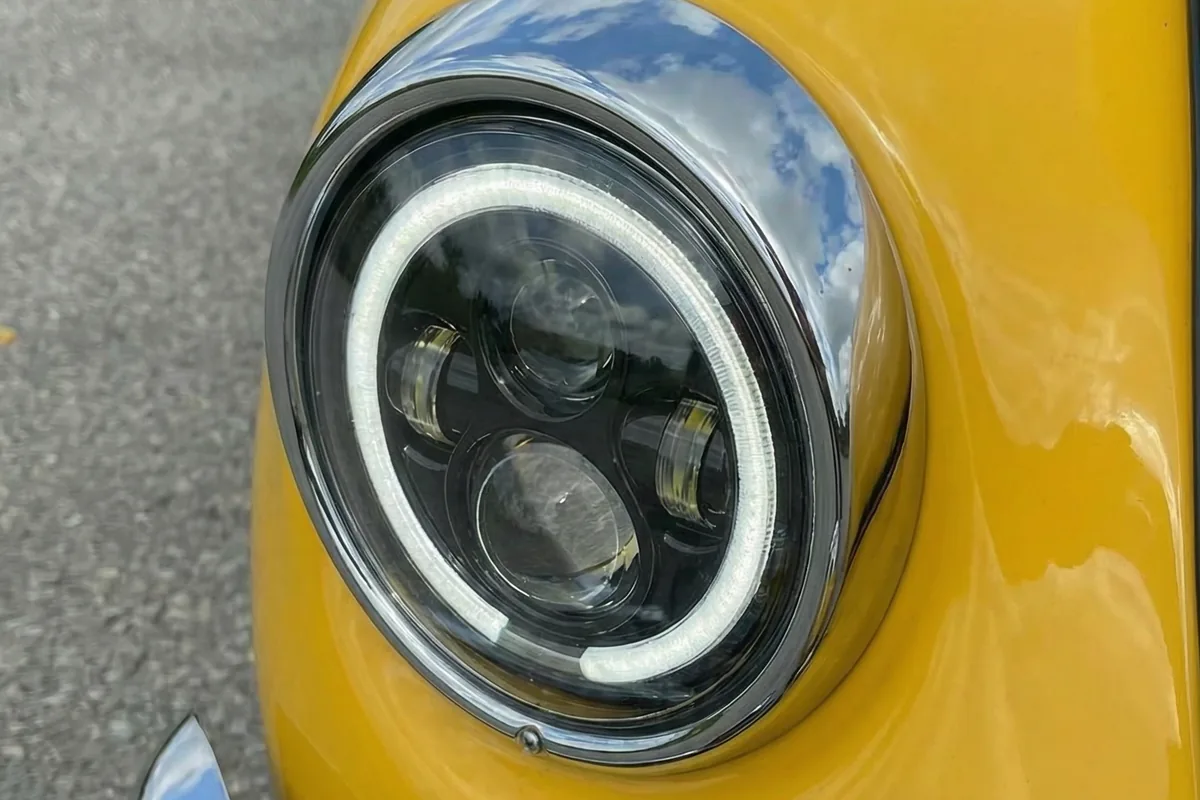 Close-up do farol dianteiro esquerdo do Fusca 911 S. Farol LED moderno com anel DRL branco e moldura cromada.