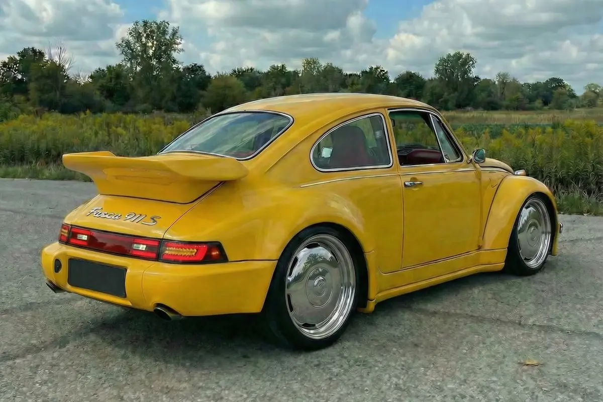 Vista traseira 3/4 do Fusca 911 S amarelo modificado. Aerofólio, lanternas estilo Porsche, rodas cromadas e para-lamas largos.