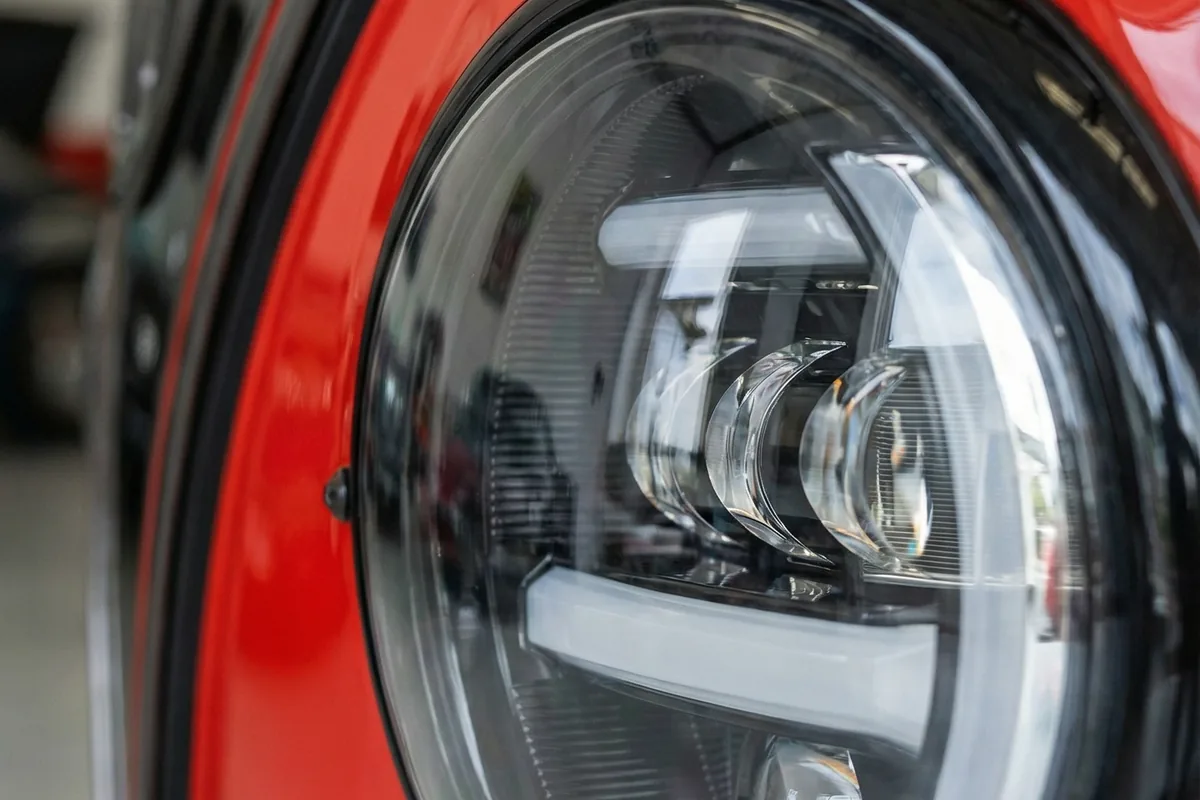 Close-up do farol dianteiro esquerdo de LED moderno e circular da Kombi Samba GLI Concept vermelha.