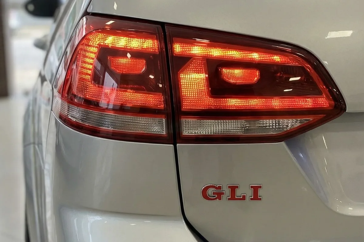 Detalhe da lanterna traseira LED acesa com o emblema GLI em vermelho e cromado no carro prateado.