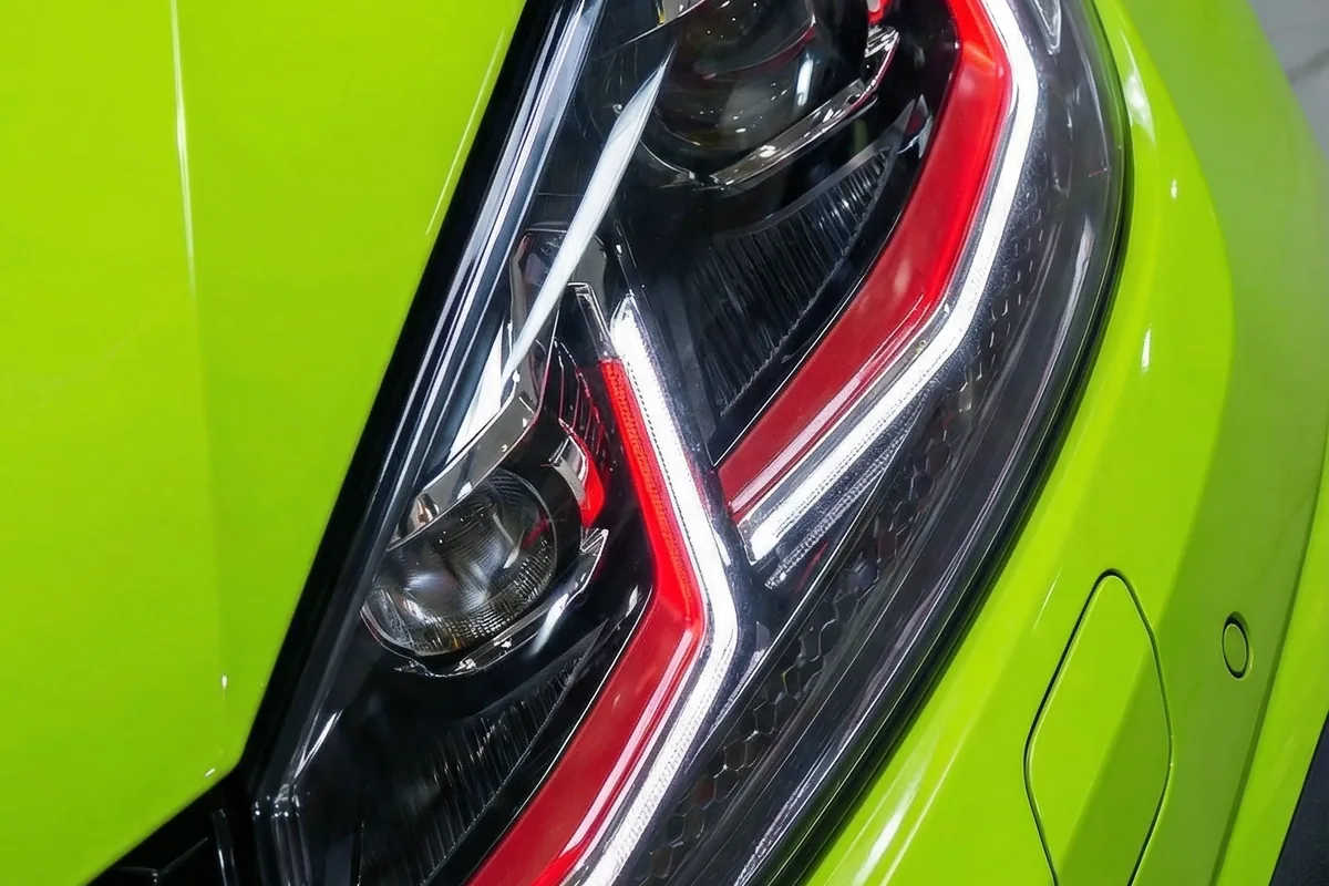 Close-up de farol LED moderno com detalhes em vermelho e branco, embutido na carroceria verde-limão.