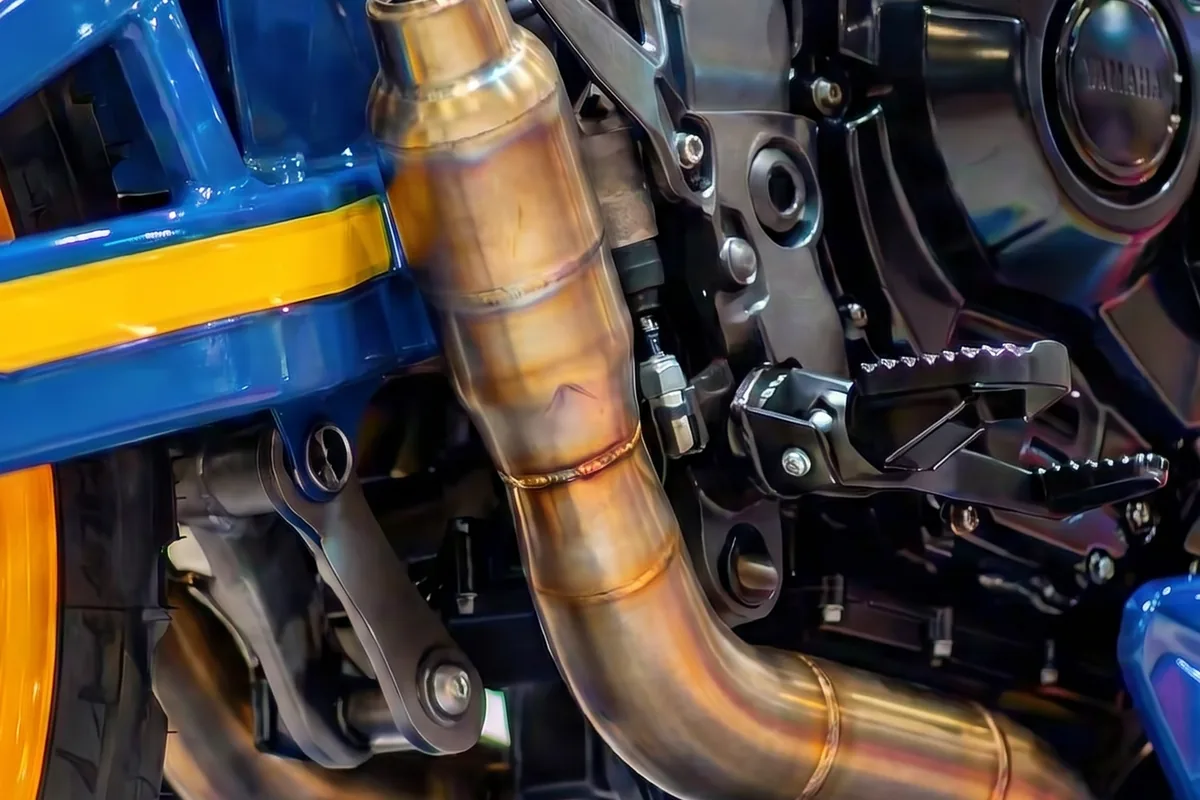 Close-up do escapamento em bronze, pedaleira off-road e parte do motor da Yamaha Tenere 600 Concept.